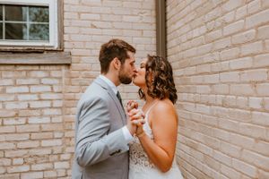 Couple shares intimate moment against brick wall background.