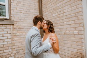 A romantic moment between newlyweds against a light brick wall backdrop.