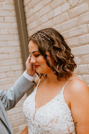 Close-up of bridal hairstyle featuring intricate braiding and soft waves against brick wall.