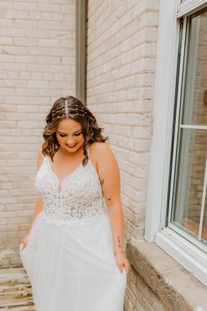 A wedding dress with delicate lace detailing and flowing tulle skirt against a white brick wall.