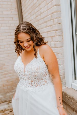 A bride smiling in a detailed lace wedding dress with delicate hair accessories.