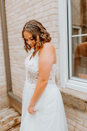A bride with curled hair and lace detailed dress smiles while looking down on her wedding day.