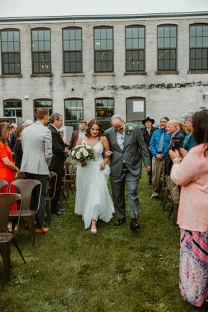 Outdoor wedding ceremony in front of an industrial brick building with arched windows.