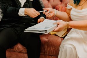 Close up view of signing wedding documents on a brown leather couch.