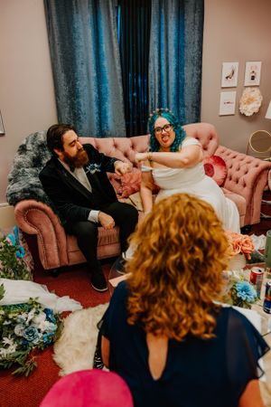 A couple relaxes on a pink velvet couch during their wedding celebration.