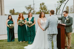 Outdoor wedding ceremony with bridal party in emerald green dresses standing at the altar.