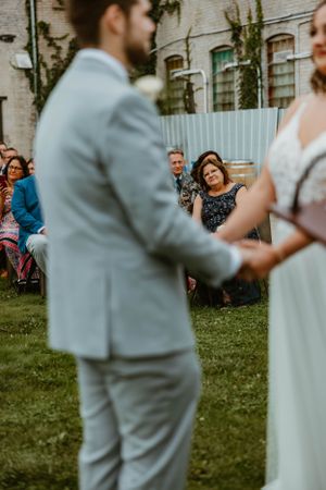 Outdoor garden wedding ceremony with guests seated on lawn watching couple exchange vows.