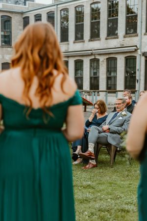Wedding guests seated on chairs during outdoor ceremony with historic building backdrop.