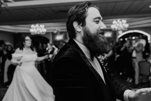 A bearded man dancing at a wedding reception in a formal black suit and bow tie.
