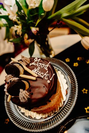 Chocolate dessert with cookies and cream toppings on a decorative glass plate near white tulips.