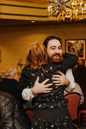 A warm embrace shared during a celebration under an elegant chandelier in a reception hall.