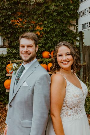 Wedding couple poses outdoors in fall scene with pumpkins and ivy covered wall.