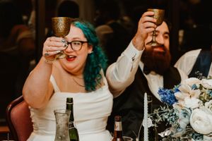 Wedding couple raises their glasses in a toast during reception with white floral centerpieces.