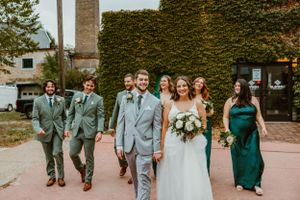 Wedding party walking together outdoors with bridesmaids in green dresses and groomsmen in gray suits.