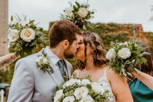 A romantic moment between newlyweds surrounded by white floral bouquets against an ivy wall.