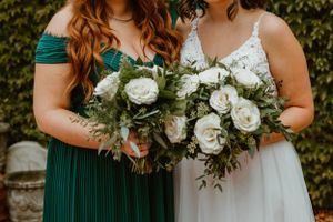 Two bouquets with white roses and greenery held against emerald green formal wear.