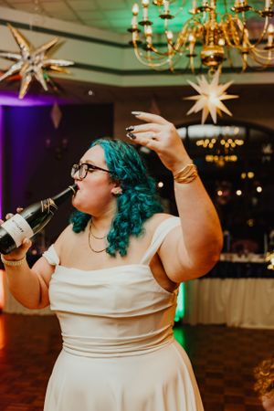 A wedding guest with bright aqua hair sings enthusiastically into a microphone during a reception.