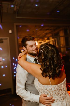 A couple shares a romantic slow dance at their wedding reception under ambient purple lighting.