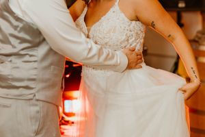 Couple in white wedding attire embrace while dancing together at a warm-lit reception venue.
