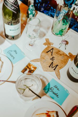 Wedding reception table with wine bottles, glasses and custom wooden A&M decor with blue place cards.