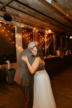 A couple shares an intimate slow dance at their wedding reception under warm string lights in an industrial venue.