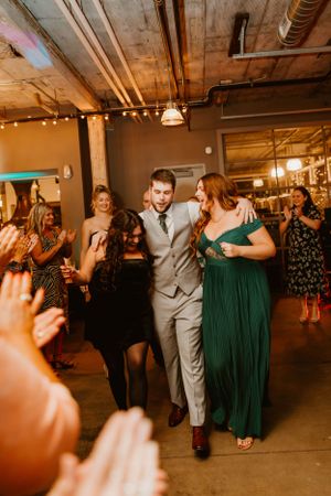 A celebration in progress at an industrial-style wedding venue with guests dancing and cheering.