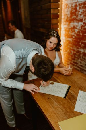 A couple reviews and signs paperwork on a wooden table at a rustic indoor venue.