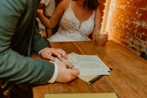 A couple reviews paperwork together at a wooden table during what appears to be a wedding ceremony preparation.