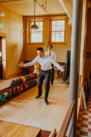 Two people having fun at a bowling alley with wooden floors and bowling balls lined up against the wall.