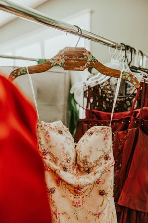 An elegant floral-patterned strapless dress hangs on a wooden hanger among other formal dresses.