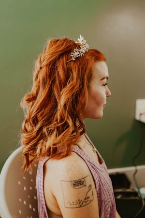A side profile shows vibrant red hair styled in waves with a delicate crystal hair accessory.