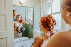 Reflection in mirror shows someone with vibrant red hair and floral tattoos getting ready on a bright morning.