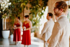 A sunlit indoor wedding venue with decorative greenery and people gathered in formal attire.