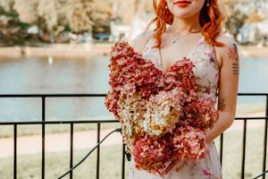A wedding bouquet of pink and cream hydrangeas held against an ocean view balcony railing.