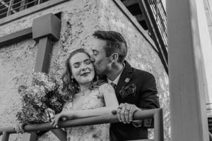Black and white wedding photograph showing a tender moment with a floral bouquet against a textured wall background.
