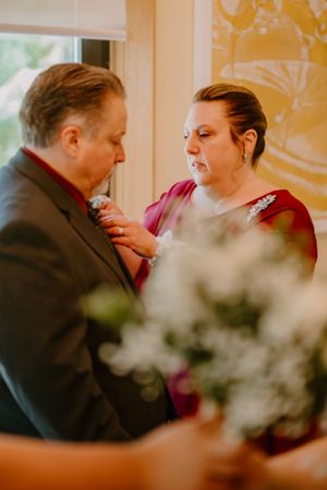 A tender moment captured during a wedding as someone helps adjust the groomsman's tie, with white flowers in the foreground.