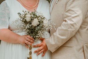Close-up of hands holding a delicate bouquet of white roses and baby's breath at a wedding ceremony.