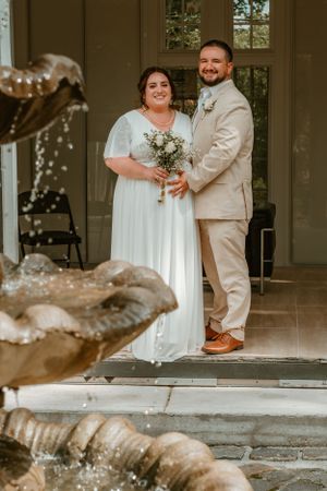 Wedding ceremony setup with ornate garden fountain in foreground and decorated entrance porch.