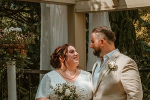 A happy couple shares an intimate moment at their outdoor garden wedding ceremony under a white pergola.