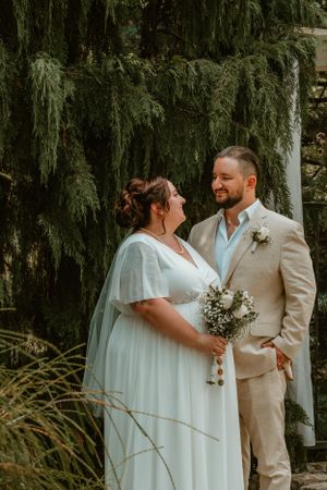 A couple shares a tender moment in front of cascading willow branches during their rustic outdoor wedding ceremony.