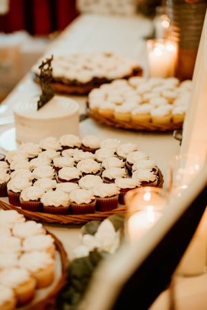 Chocolate cupcakes decorated with white frosting flowers arranged on vintage plates with glowing candles nearby.