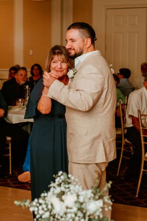 A tender dance moment at a wedding reception with guests watching in the background and white floral decorations.