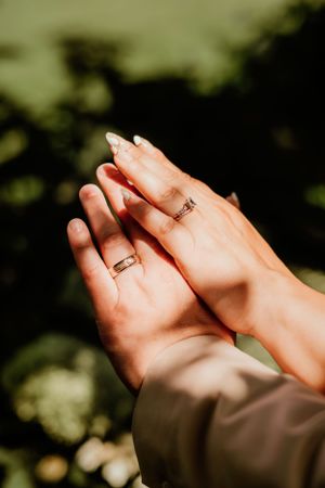 Close-up shot of hands wearing matching wedding bands with a blurred natural background.