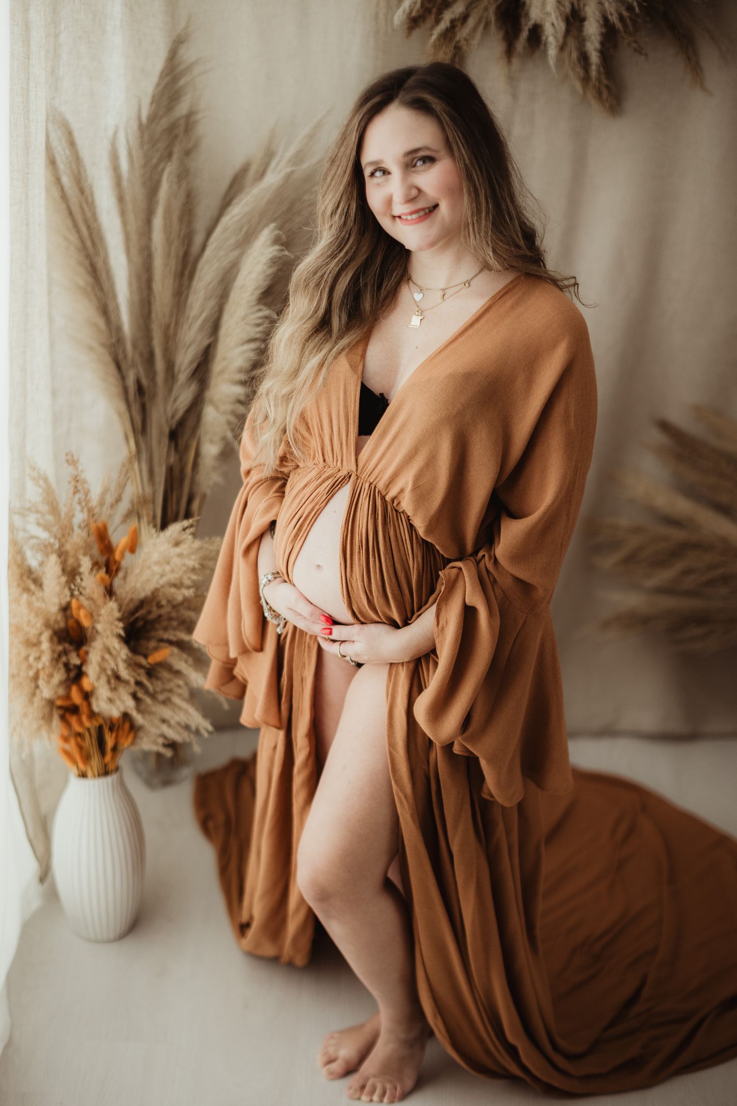 Maternity photo series in warm earth tones featuring flowing rust-colored dress and dried floral arrangements in vases.