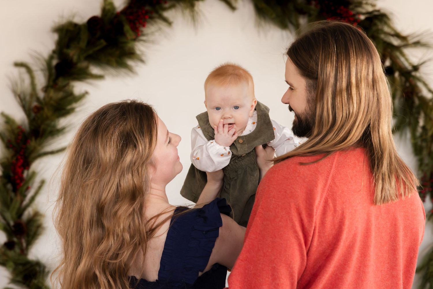 Holiday portrait showing a warm family moment with evergreen wreath decoration in the background.