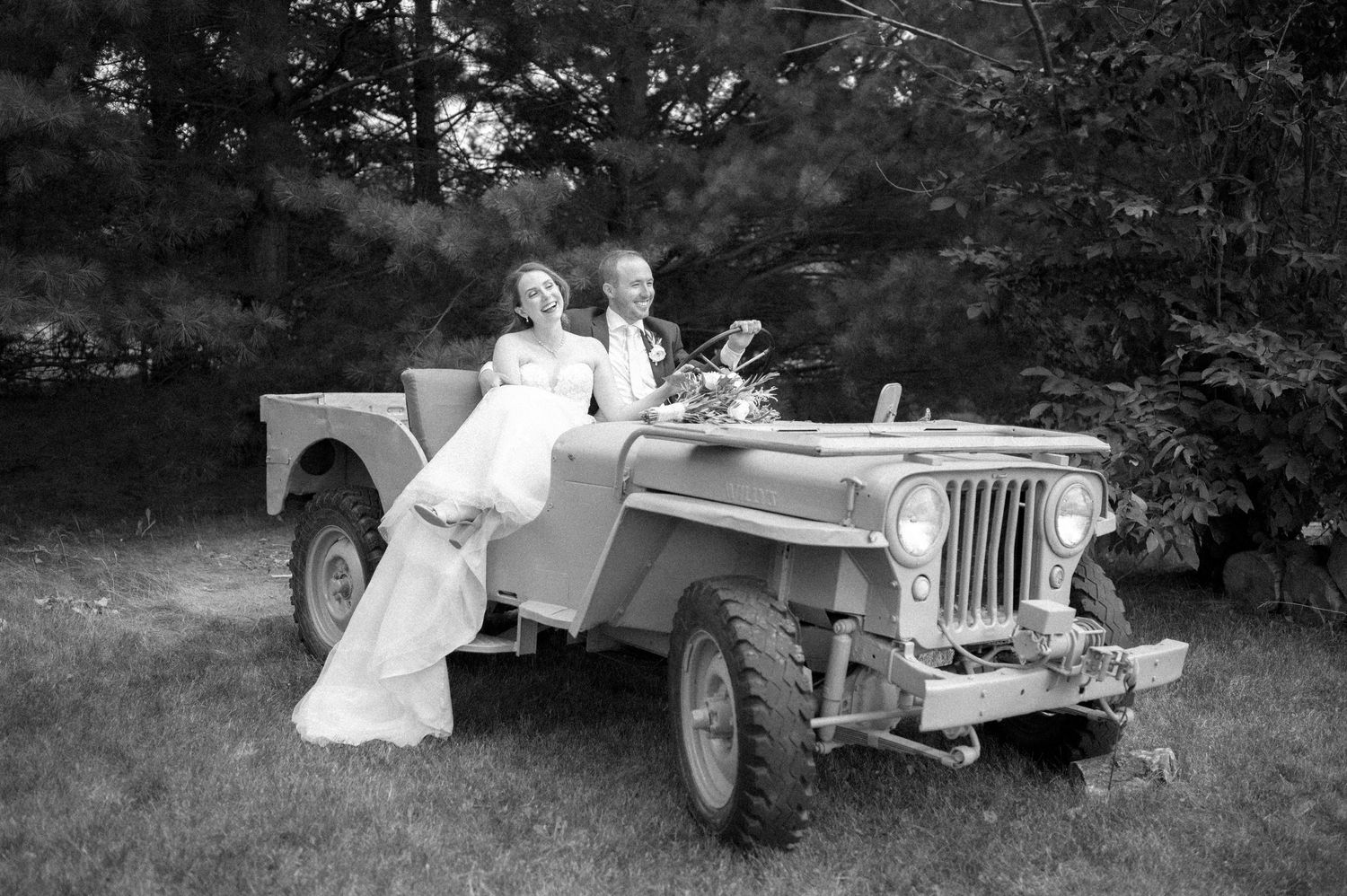 Vintage black and white photograph showing a couple posing with a classic Willys Jeep outdoors in a garden setting.