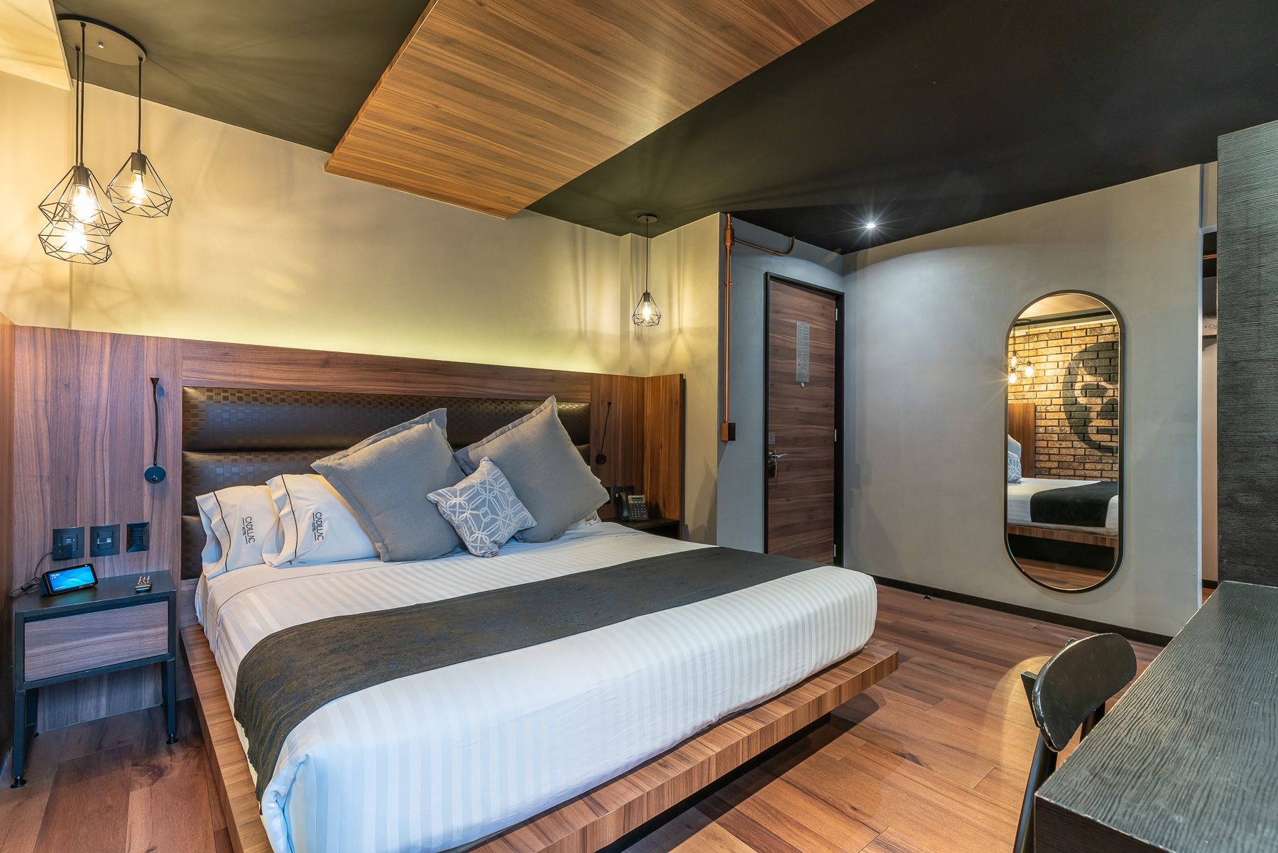 Luxurious hotel room featuring wood-paneled walls, hanging pendant lights, and a plush king bed. Cadillac Hotel Boutique CDMX.