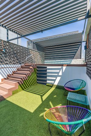 Modern rooftop terrace with striped shade covering, artificial turf, and colorful accent chairs. Cadillac Hotel Boutique.