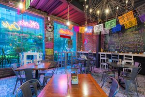 Vibrant restaurant interior with colorful neon lights, brick walls, and eclectic decor featuring casual dining tables and chairs.