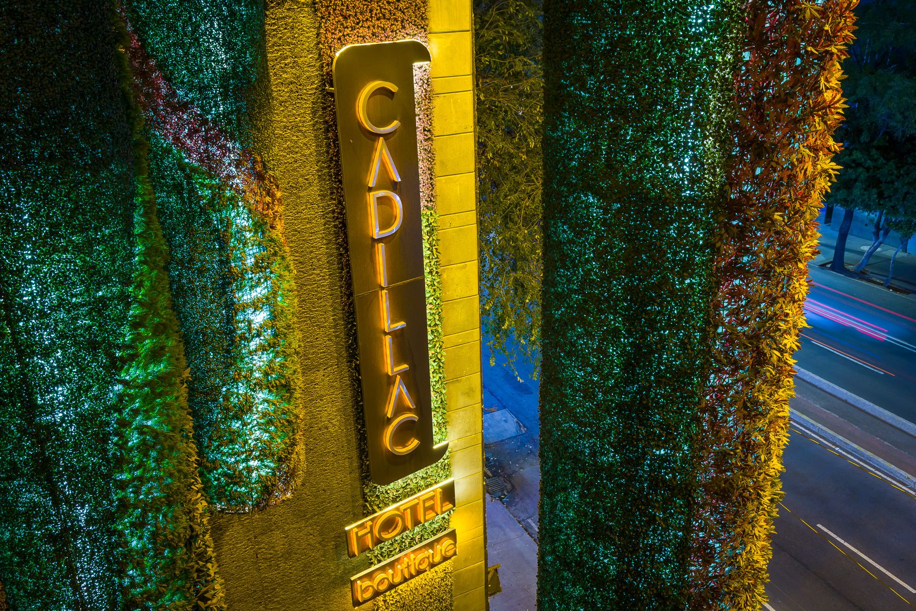 Illuminated Cadillac sign with green sparkly decorative elements on a building exterior at night. Cadillac Hotel Boutique.